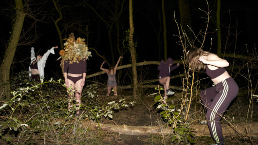 Dansende mensen in een donker bos met takken en struiken.