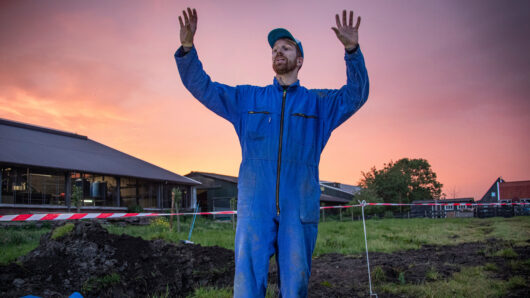 De Boer Op: boer in avondrood met zijn handen omhoog