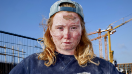 Campagnebeeld PUT: stoere meid met blond haar en blauwe kleding met verf strepen op bouwterrein.