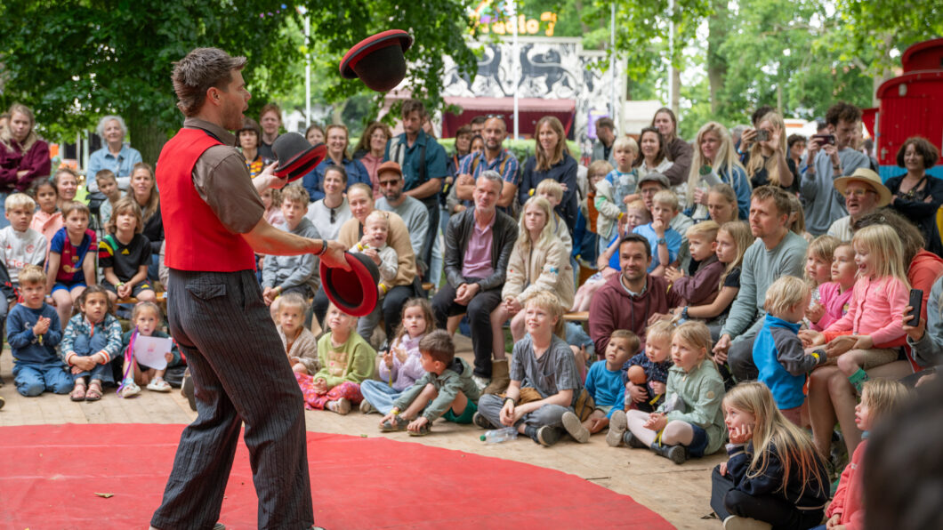 Rein de kok die jongleert met drie hoeden op de achtergrond zie je publiek zitten