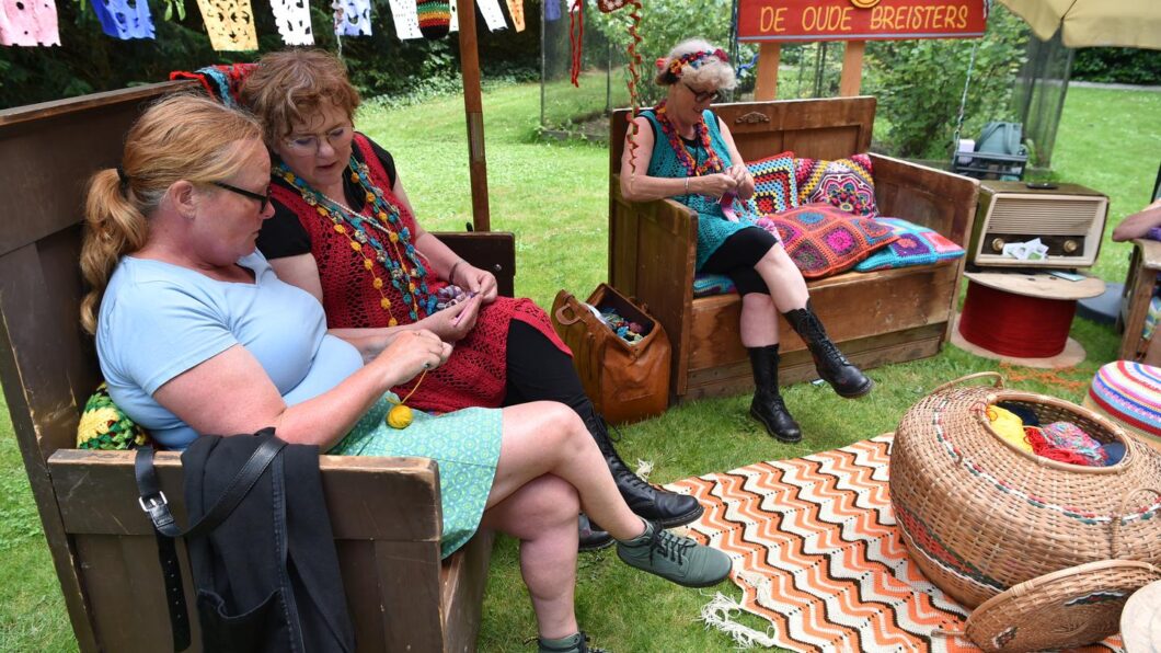 De oude breisters zitten te breien met een bezoeker tijdens Volbloeiers