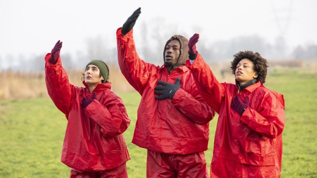 3 dansers met rode regenpakken op een weiland