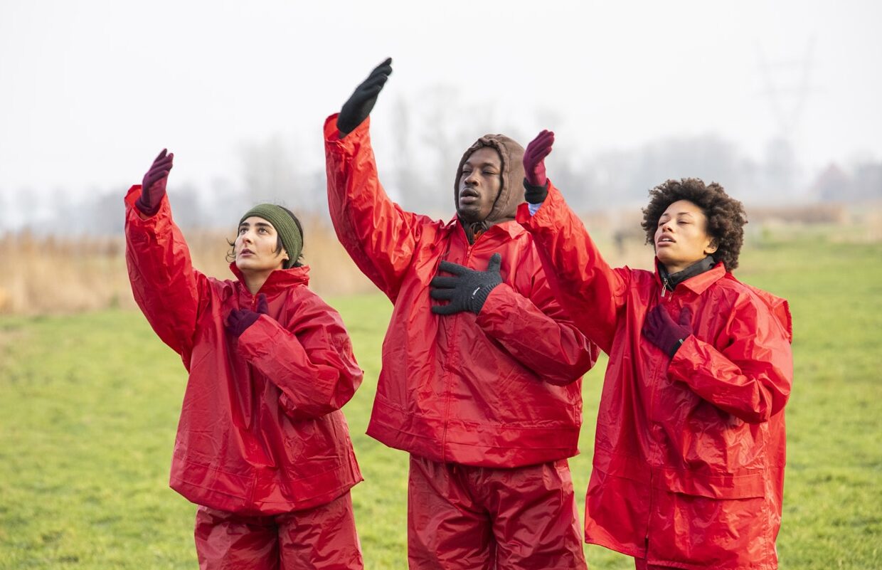 3 dansers met rode regenpakken op een weiland