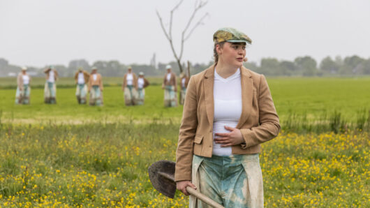 Dit Verdronken Land - vrouw staat in het land met op de achtergrond een koor dat een boom plant