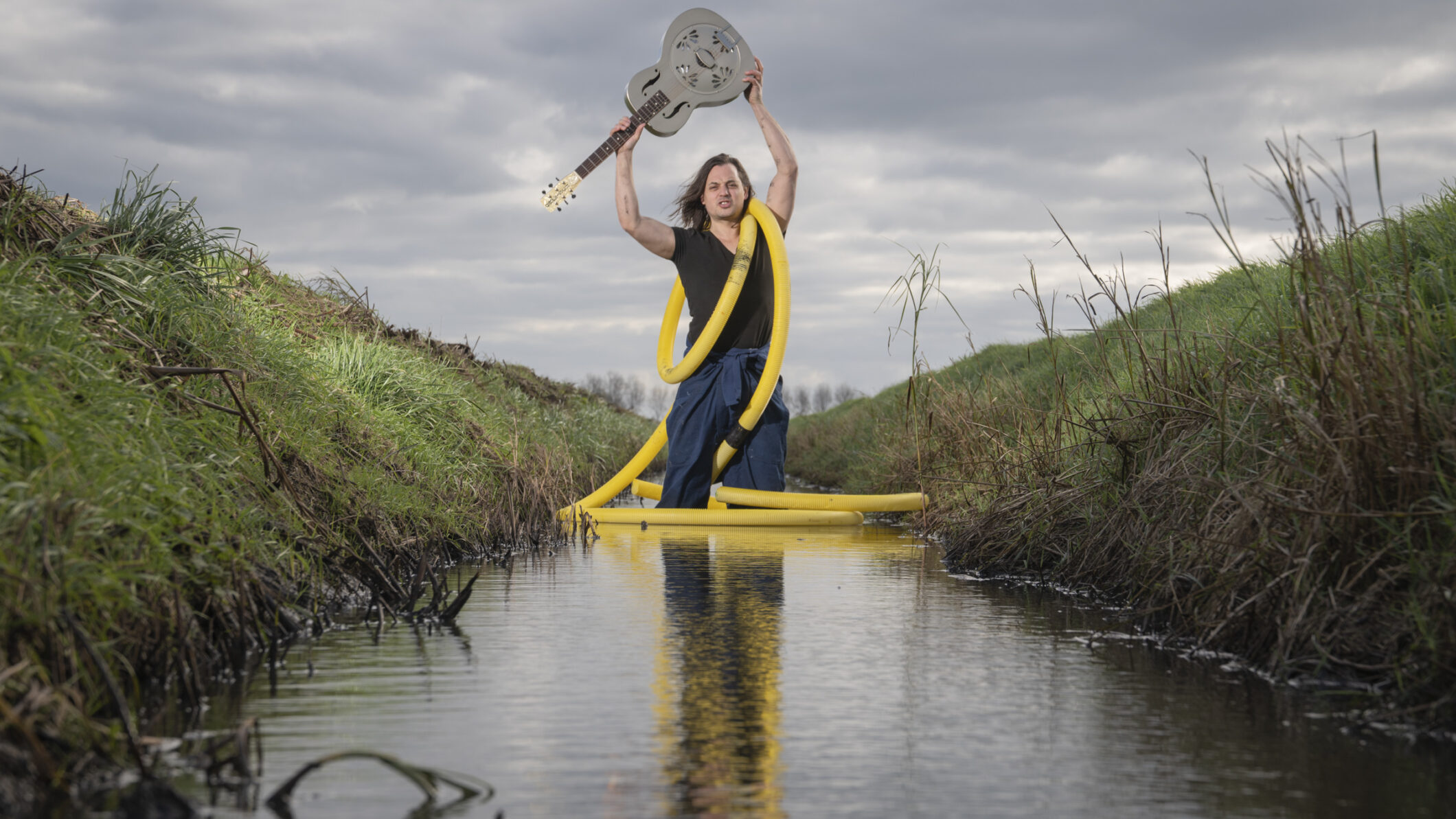 Dit Verdronken Land - man in een sloot houdt boven zijn hoofd een gitaar in de hand