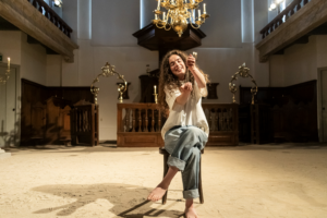 Anna an Sich - vrouw in een kerkje zit op een stoel en laat zand door haar handen glijden