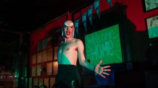 Op de foto Sytze Bouma als drag voor een bord met 'welcome home' erop - scenefoto van de voorstelling Drag me Home